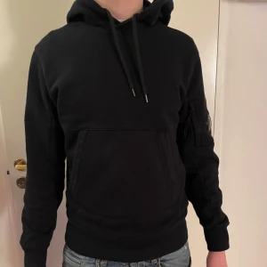 Svart CP Company hoodie - Säljer nu en snygg svart CP Company hoodie som är i grymt skick och ändast använd ett fåtal gånger. Inköpt på Thernlunds i Stockholm och nypris på denna ligger på ca 2700 kr. Personen på bilden är 177 cm och väger 65 kg. Kvitto finns! Hör av dig vid frågor!