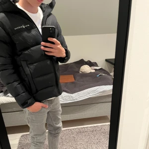 Svart dunjacka från Sailracing  - Säljer en svart dunjacka från Sailracing i mycket bra skick. Jackan är perfekt för vintern. Den har en dragkedja framtill och är fylld med 80/20 dun för extra värme. Perfekt för kalla dagar! Passar dig mellan s-Xs då den är barnstorlek