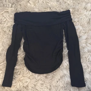 Svart offshoulder topp från SHEIN - Svart offshoulder topp från SHEIN med långa ärmar och bred, vikt kant upptill. Toppens material är en blandning av polyester och polyamid, vilket ger en mjuk och stretchig känsla. Snygg och enkel design som är lätt att matcha med olika outfits.