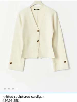 Krämvit stickad kofta med knappar - Snygg krämvit stickad kofta från Gina Tricot med v-ringning och stora bruna knappar framtill och vid ärmsluten. Koftan har en rak, något boxig passform och långa ärmar. Perfekt för lager-på-lager och enkel att styla. Knappt använd. Mycket bra skick!