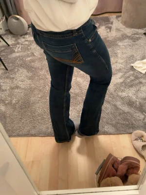 Mörkblå bootcut jeans med brodyr - Mörkblå snygga jeans med orangea sömmar från HM, low waist. Inte använda på länge och dom har bara använts i typ ett halvår, så inga fula märken elle så!!🥰🥰