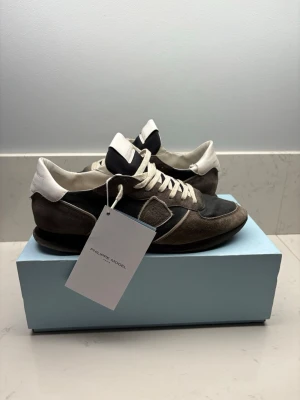 Philippe Model svarta sneakers - Kom gärna med prisförslag! Snygga sneakers från Philippe Model i svart och mörkbrunt med vita detaljer och vita skosnören. Ovandelen är i mocka och textil, med en vit hälkappa och klassisk låg profil. Perfekta för dig som gillar stilrena och tidlösa sneakers. Org pris 3800kr+!