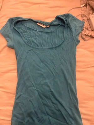 Ljusblå ribbad topp från Kappahl - Säljer en ljusblå ribbad topp från Kappahl i storlek XS. Toppen har korta ärmar, rund halsringning och är tillverkad i ett mjukt, stretchigt material som sitter snyggt på kroppen. Perfekt att styla med jeans eller kjol.