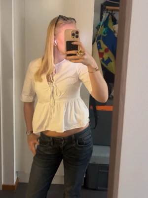 Vit blus med knytning från H&M - Söt vit blus från H&M med knytning framtill och lätt rynkad midja. Blusen har rund halsringning och trekvartsärm. Tillverkad i ett tunt, vävt material som känns luftigt och fräscht.