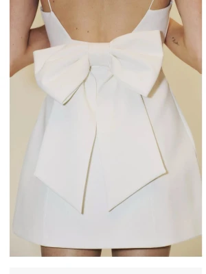 Vit kort klänning med stor rosett - Supersöt vit miniklänning med en stor dekorativ rosett framtill. Klänningen har axelbandslös design och är gjord i stretchigt material som ger en smickrande passform. Perfekt för dig som vill sticka ut med en trendig och lekfull look. Jag säljer den för den var för liten för mig. Helt slutsåld på Zara. Banden är av det är det enda. Jag tycker att den är finare utan band med