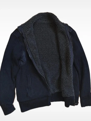 Mörkblå stickad kofta med foder - Mysig mörkblå stickad kofta med dragkedja och två fickor framtill. Insidan är fodrad med mjuk teddy som gör den extra varm och skön. Perfekt för kyliga dagar och har en stilren, enkel design med ribbade muddar vid ärmar och nederkant.