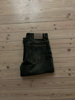 Our legacy jeans - Säljer ett par svarta jeans med bootcut passform och klassisk femficksdesign. Jeansen har en mörk tvätt och är perfekta för en avslappnad stil. Materialet är denim och de har en enkel bakficka utan synliga detaljer.