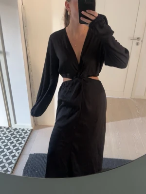 Svart långklänning med cut-out - Svart långklänning med v-ringning och långa ärmar. Klänningen har en cut-out i midjan. 