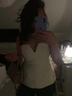 Vit korsett-topp med v-ringning - Snygg vit korsett-topp med markerad v-ringning och figurnära passform. Toppen är ärmlös och har en stilren, elegant look som passar perfekt till jeans eller kjol. Perfekt för dig som vill ha en trendig och chic outfit.