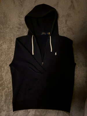 Navy blue zip hoodie från Polo Ralph Lauren - Säljer denna tvär feta mörkblåa zip hoodie från Polo Ralph Lauren med dragkedja, vit logga på bröstet och vita snören i huvan som ger den en unik look från de andra zip hoodie från Ralph Lauren, det är storlek M men skulle säga att de skulle funka bra som storlek S oxå, hör av er vid funderingar!!