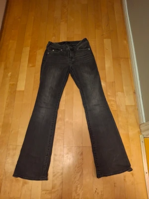 Svarta bootcut jeans True Religion - Säljer ett par svarta bootcut jeans från True Religion med snygga detaljerade bakfickor och silverknappar. Jeansen har klassisk femficksdesign och är tillverkade i denim med lätt tvättad look. Perfekta för dig som gillar en avslappnad men trendig stil.