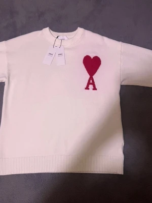 Vit Ami Paris knit  - Snygg vit stickad tröja från Ami Alexandre Mattiussi med röd hjärtloggan  och bokstaven A på bröstet. 100% bomull en bild med  står att den är de