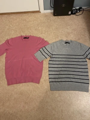 Två basic tröjor, rosa & grå-randig - Säljer två stilrena tröjor. En i helrosa med rund hals och ribbade muddar, samt en ljusgrå med svarta horisontella ränder och kortare ärmar. Perfekta till jeans eller kjol för en enkel och clean look.