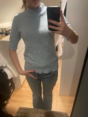 Ljusblå stickad topp med polokrage - Snygg ljusblå stickad topp med polokrage och halvlånga ärmar. Tröjan har ribbade muddar vid ärmslut och nederkant.