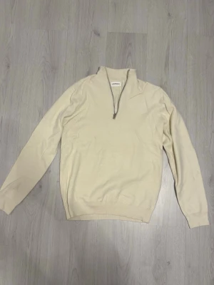 Beige stickad tröja med halvzip Lindbergh - Beige stickad tröja från Lindbergh med halv dragkedja vid halsen. Tröjan har långa ärmar, ribbade muddar och är gjord i ett mjukt material. Enkel och clean design som är lätt att styla till olika looks.