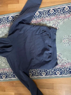 Mörkblå hoodie med magficka - Snygg mörkblå hoodie med klassisk huva och stor magficka framtill. Perfekt för en avslappnad stil och enkel att matcha med jeans eller joggers. Mjuk bomullskänsla och ribbade muddar vid ärmslut och nederkant.