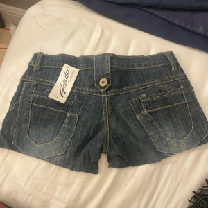 Mörkblå jeansshorts från Avdor Fashion - Snygga mörkblå jeansshorts från Avdor Fashion med coola detaljer som dekorativa knappar och fickor både fram och bak. Klassisk femficksmodell med bälteshällor och kontrastsömmar. Perfekta för sommaren och ger en avslappnad vibe.