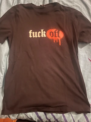 Svart t-shirt med tryck - Cool svart t-shirt med trycket 'fuck off' i vitt och rött framtill. Texten har en spraymålad effekt med droppar runt ordet 'off'. Klassisk passform och rund halsringning. Perfekt för dig som vill sticka ut med din stil. Perfekt för t-shirt som pyjamas.