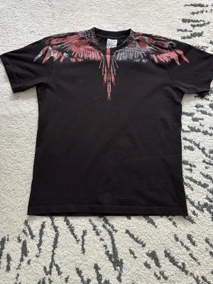 Svart t-shirt från Marcelo Burlon - Cool svart t-shirt från Marcelo Burlon med ikoniskt fjädermönster i rött, blått och grått runt halsen. T-shirten har rund hals och korta ärmar, perfekt för en trendig streetwear-look.