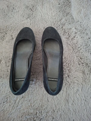 Svarta kilklackade pumps Vagabond - Snygga svarta pumps från Vagabond med kilklack och rundad tå. Skorna är i mockaimitation och har en stilren, klassisk design som passar till många olika looks. Perfekta för dig som vill ha både höjd och komfort.