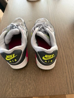 Nike Air Max 90 grå/neon sneakers - Nike Air Max 90 sneakers i grå mesh och syntet med detaljer i svart, neon och rosa. Klassisk chunky sula och tydlig Nike Air-logga bak. Skorna har vita snören med neonfärgade detaljer och en ikonisk retrostil som sticker ut.