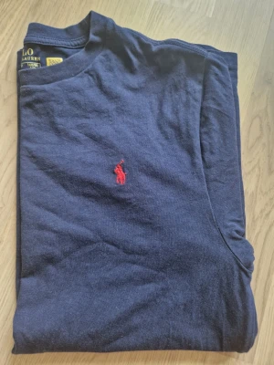 Ralph lauren t-shirt - Marin blå t-shirr med röd logga. Använd 2 gånger så väldigt bra skick. Storleken är L 14-16 vilket motsvarar en XS