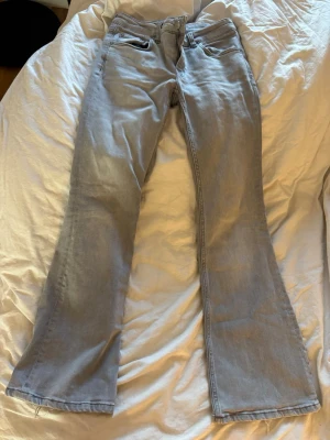 Ljusblå bootcut jeans - Säljer ett par ljusblå bootcut jeans med klassisk femficksdesign och råa kanter längst ner. Jeansen har en avslappnad passform och är tillverkade i denim. Perfekta för dig som gillar en retroinspirerad look.