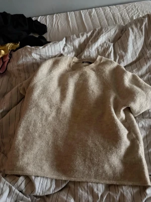 Beige stickad tröja med kort ärm - Mysig beige stickad tröja med korta ärmar och rund halsringning. Tröjan har en avslappnad passform och ribbstickade detaljer vid halsen. Perfekt för lager på lager och enkel att matcha med olika stilar.