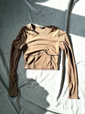 Brun ribbad croppad topp - Trendig croppad topp från i brun ribbat material. Långärmad modell med markerade sömmar och rund halsringning. 