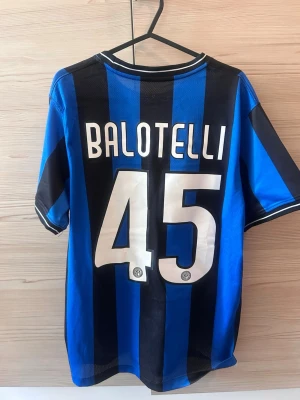 Inter Milan Balotelli matchtröja - Säljer en blå och svart randig Inter Milan matchtröja från Nike med Balotelli och nummer 45 på ryggen. Tröjan har officiellt klubbmärke, Pirelli som sponsor och Champions League-finaltext på bröstet. Tillverkad i lätt och ventilerande material, perfekt för fotboll eller samling.