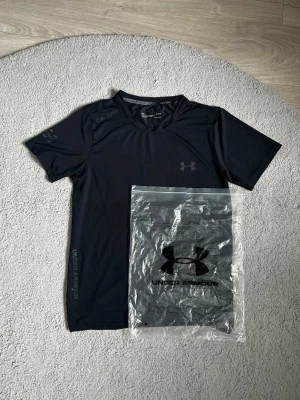 Svart träningströja Under Armour - Snygg svart träningströja från Under Armour med korta ärmar och rund hals. Tillverkad i ett lätt och snabbtorkande funktionsmaterial, perfekt för intensiva träningspass. Diskret logga på bröstet och tryck på ärmen.Väldigt fin och bra för sommaren och för träningen. Fraktar så fort du har köpt🚚📦Aktiv 24/7✅ Hör av dig via frågor⁉️