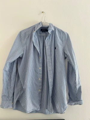 Blårandig skjorta från Polo Ralph Lauren - Klassisk blårandig skjorta från Polo Ralph Lauren med button-down krage och broderad logga på bröstet. Skjortan har långa ärmar, vita knappar och är tillverkad i mjuk bomull. Perfekt för en clean och stilren look. Passar nog bäst dig som är ca 165, size S. Bara att skriva vid frågor!! 🦦🚀