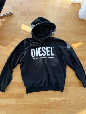 Svart hoodie från Diesel med tryck - Svart hoodie från Diesel med stort vitt logotryck på bröstet och texten 'For Successful Living'. Klassisk modell med huva och dragsko, samt ribbade muddar vid ärmslut och nederkant. Perfekt för en avslappnad och cool stil.