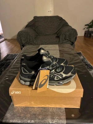 Svarta Asics sneakers med silverdetaljer - Snygga svarta Asics sneakers med silvriga detaljer och meshpaneler för bra ventilation. Skorna har en chunky sula och klassisk snörning. Perfekta för dig som gillar sportig och trendig stil. Levereras med originalkartong och tag kvar.