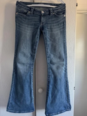 Blå bootcut jeans från Gina Tricot - Snygga blå bootcut jeans från Gina Tricot med klassisk femficksdesign och låg midja. Jeansen har en lätt tvättad look och utsvängda ben, perfekta för en avslappnad och trendig stil. Materialet är mjukt denim med stretch för extra komfort.