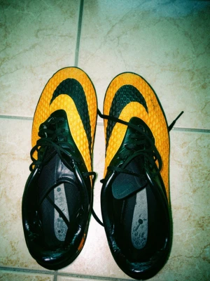 Nike Hypervenom orange fotbollsskor - Säljer ett par Nike Hypervenom fotbollsskor i orange och svart med coolt bikakemönster på ovandelen och stora Nike-loggor. Skorna har dobbar för bra grepp på planen och en dödskalle-detalj på hälen. Tillverkade i syntetmaterial och designade för grym bollkontroll.