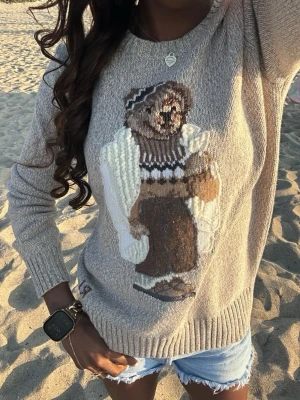 Beige stickad tröja med björnmotiv - Stickad beige tröja med ett stort björnmotiv framtill. Tröjan har ribbade muddar vid ärmslut och nederkant samt en avslappnad passform. Perfekt för dig som gillar gulliga detaljer och vill ha något mysigt och trendigt i garderoben. storlek S. Prislapp finns