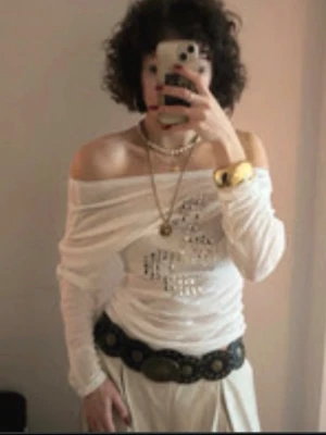 Vit offshoulder topp med nitar - Trendig vit offshoulder topp med långa ärmar och coolt mönster av silvriga nitar framtill. Nitarna visar en musik logga. Tunt och lätt material som ger en snygg draperad effekt över axlarna. Passar S-M enligt mig.