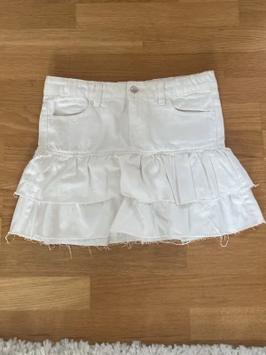 Vit volangkjol med jeansdetaljer - Säljer en kort vit jeanskjol med volanger. Jag säljer den eftersom den är för stor för mig. Perfekt för sommaren💗