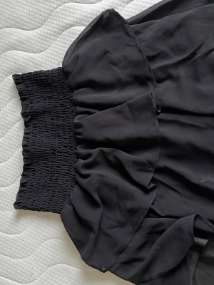 Svart volangkjol från Chelsea - Supersnygg svart kortkjol från Chelsea med bred smock i midjan och volangdetaljer. Storlek Xs men passar upp till M då den är stretchig 
