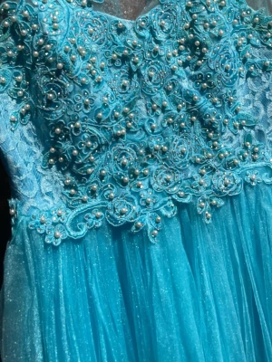 Blå långklänning med pärlor och spets - Magisk blå långklänning med glittrande tyllkjol och överdel dekorerad med spets, pärlor och broderade detaljer. Ärmlös modell med rund halsringning och transparent mesh upptill. Perfekt för bal eller student.det står stolen XL på den men den är som M 