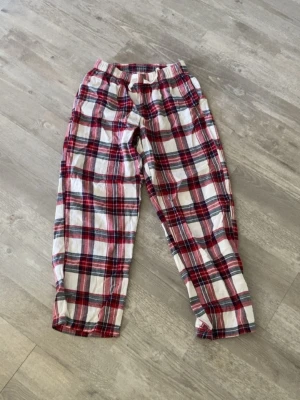 Rutiga pyjamasbyxor i bomull - Säljer ett par klassiska pyjamasbyxor med rött, vitt och svart rutmönster. Byxorna har resår i midjan för extra komfort och är tillverkade i mjuk bomull. Perfekta för mysiga hemmakvällar eller lata morgnar.