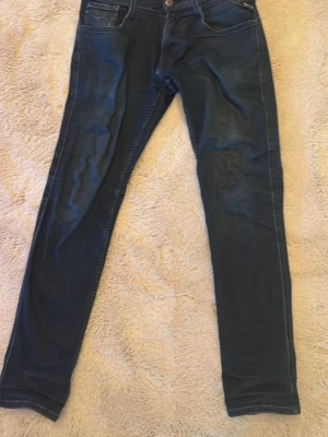 Mörkblå replay jeans - Snygga mörkblå slim fit jeans från Lee med klassisk femficksdesign och diskreta slitningar. Jeansen har smal passform och är tillverkade i stretchigt denimtyg för extra komfort. Perfekta för en trendig och avslappnad look. (Har ett litet hål i den lilla fickan där fram på höger sida)