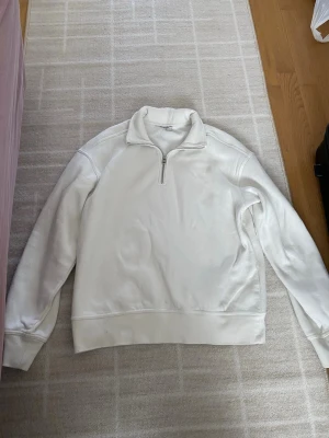 Vit hoodie med half zip - Klassisk vit hoodie med half zip och hög krage. Hoodien har långärmad design och ribbade muddar vid ärmslut och nederkant. Perfekt för en clean och enkel stil.