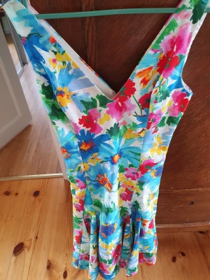Blommig klänning från Polo Ralph Lauren - Färgstark blommig klänning från Polo Ralph Lauren med v-ringning och ärmlös design. Klänningen har en figurnära passform upptill och en lätt utställd kjol. Materialet känns svalt och passar perfekt till varma dagar. Dragkedja i sidan för enkel påklädning.