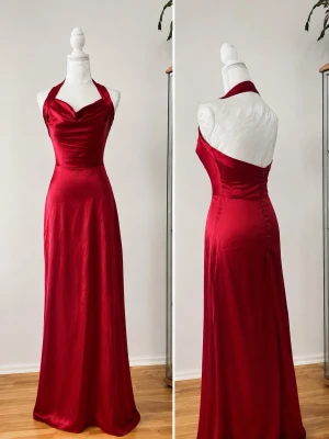 Röd långklänning i satin med halterneck - Elegant röd långklänning i glansigt satinmaterial med halterneck och öppen rygg. Klänningen har figurnära passform och svepande kjol som ger en lyxig känsla. Perfekt för speciella tillfällen.