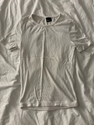 Vit ribbad t-shirt från Gina Tricot - En stilren vit ribbad t-shirt från Gina Tricot i storlek XXS. T-shirten har korta ärmar, rund halsringning och är tillverkad i ett mjukt bomullsmaterial. Perfekt basplagg att matcha med allt i garderoben.