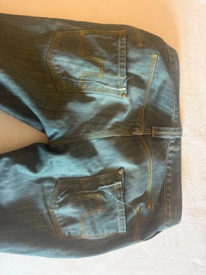 Blå jeans från J. Lindeberg - Snygga blå jeans från J. Lindeberg med klassisk femficksdesign och kontrastsömmar. Jeansen har raka ben och tydliga bakfickor med dekorativa sömmar. Perfekta för en stilren och avslappnad look. De är omsydda från baggy till botcut vilket drog ner priset
