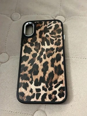 Leopardmönstrat mobilskal i svart och beige - Snyggt mobilskal med leopardmönster i svart och beige. Skalets kanter är svarta. Materialet är plast med en matt finish. Ena silver detaljen har låsnat där man sänker ljudet på mobilen. Annars jätte bra skick!