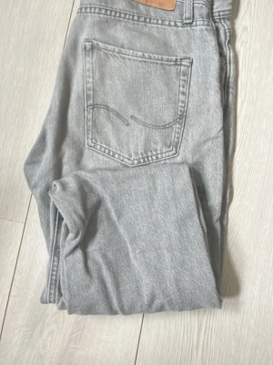 Grå jeans från Jack & Jones - Snygga grå jeans från Jack & Jones med klassisk femficksdesign och raka ben. Jeansen har en ljusgrå tvätt och är tillverkade i bomull. Perfekta för en avslappnad och trendig stil.